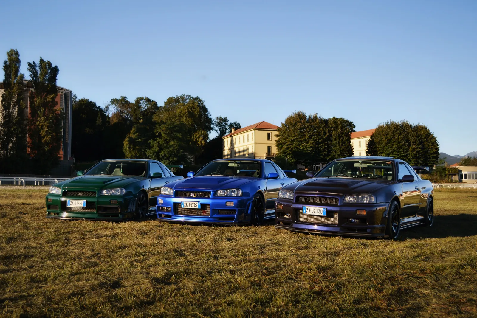 Tre Nissan Skyline GT-R verde, blu e viola parcheggiate in un prato