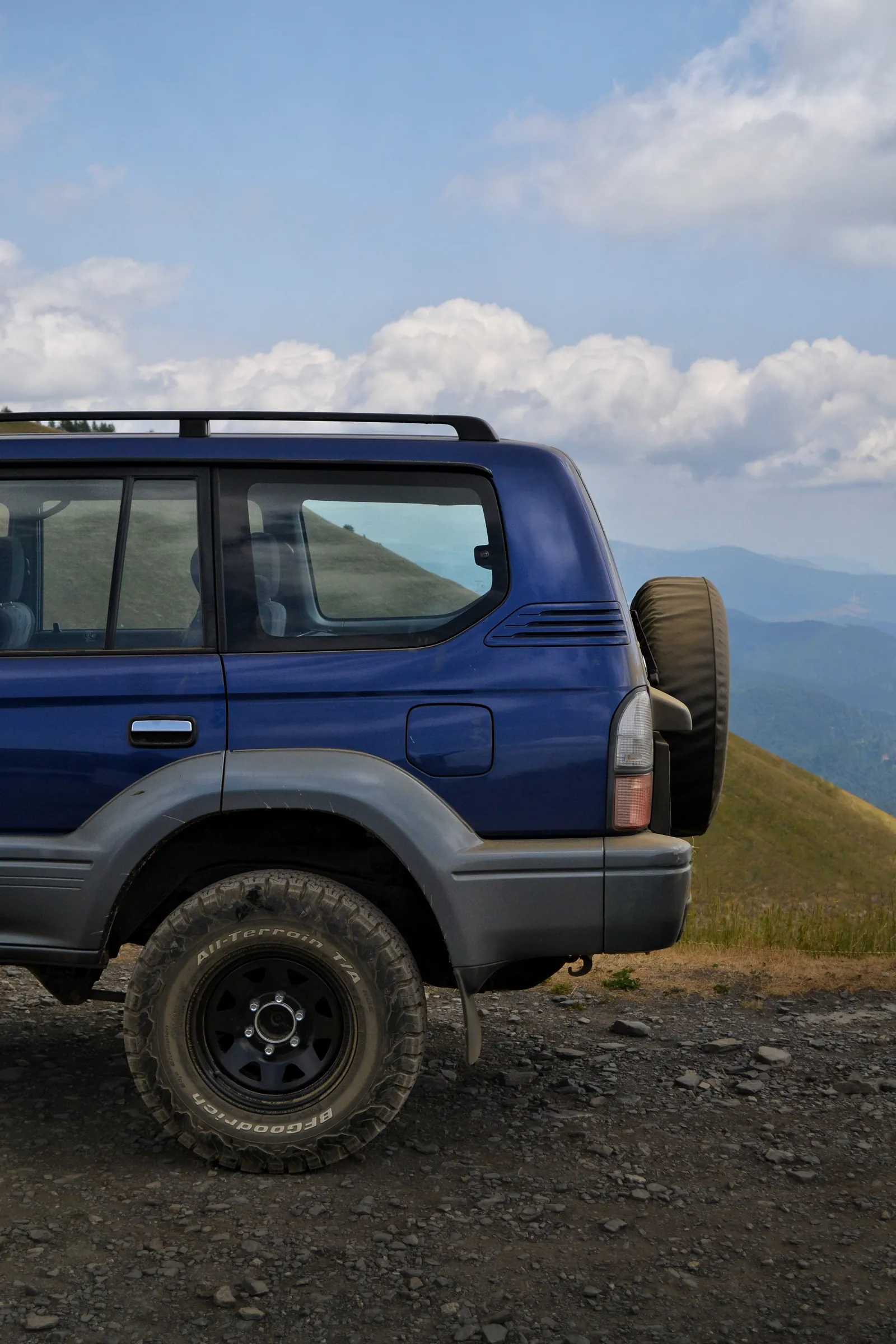 SUV fuoristrada blu con ruota di scorta posteriore su uno sterrato di montagna