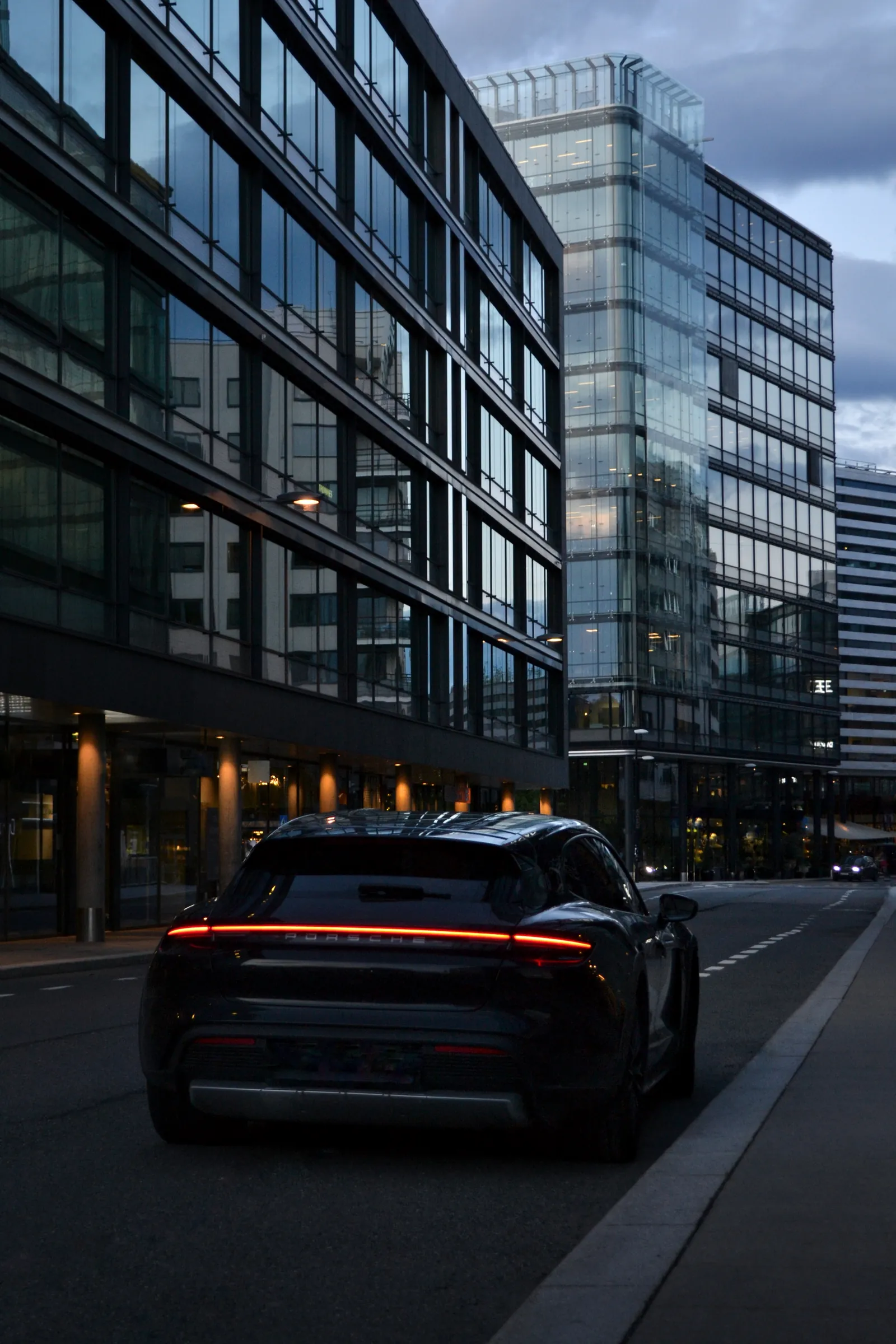 Porsche scura con fanale a barra luminosa in una strada cittadina al tramonto