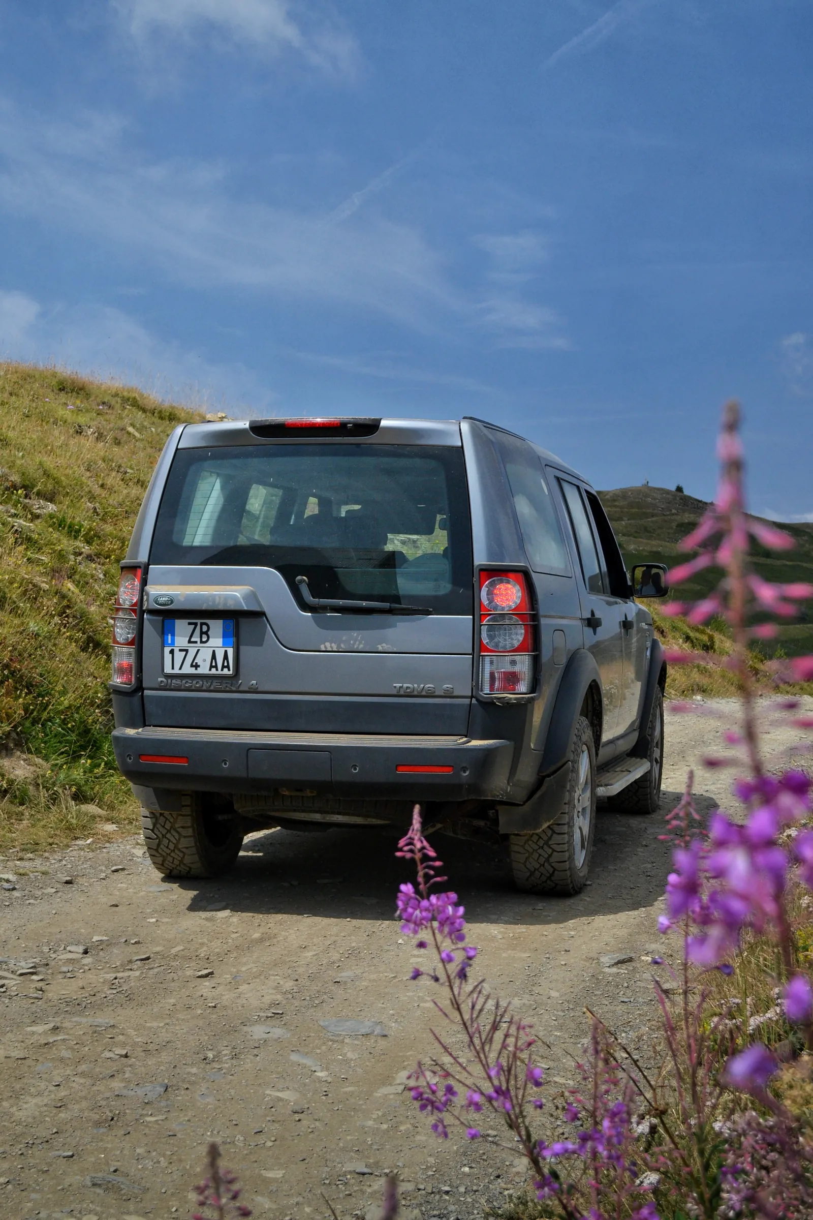 Land Rover Discovery vista da dietro su uno sterrato di montagna con fiori selvatici