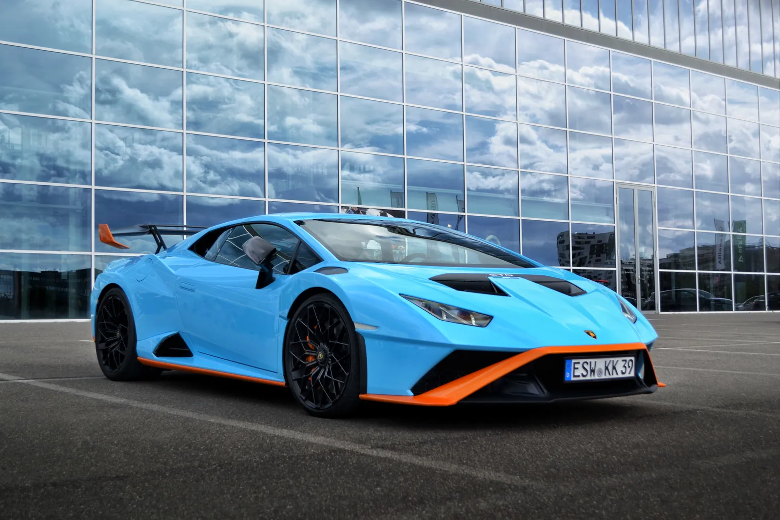 Lamborghini Huracán STO azzurra con dettagli arancioni davanti a un edificio in vetro