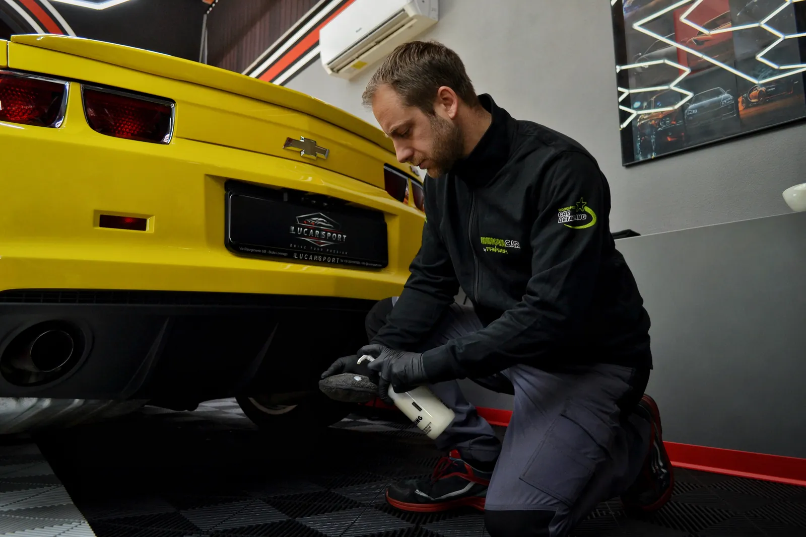 Detailer al lavoro sul posteriore di una Chevrolet Camaro gialla in un'officina