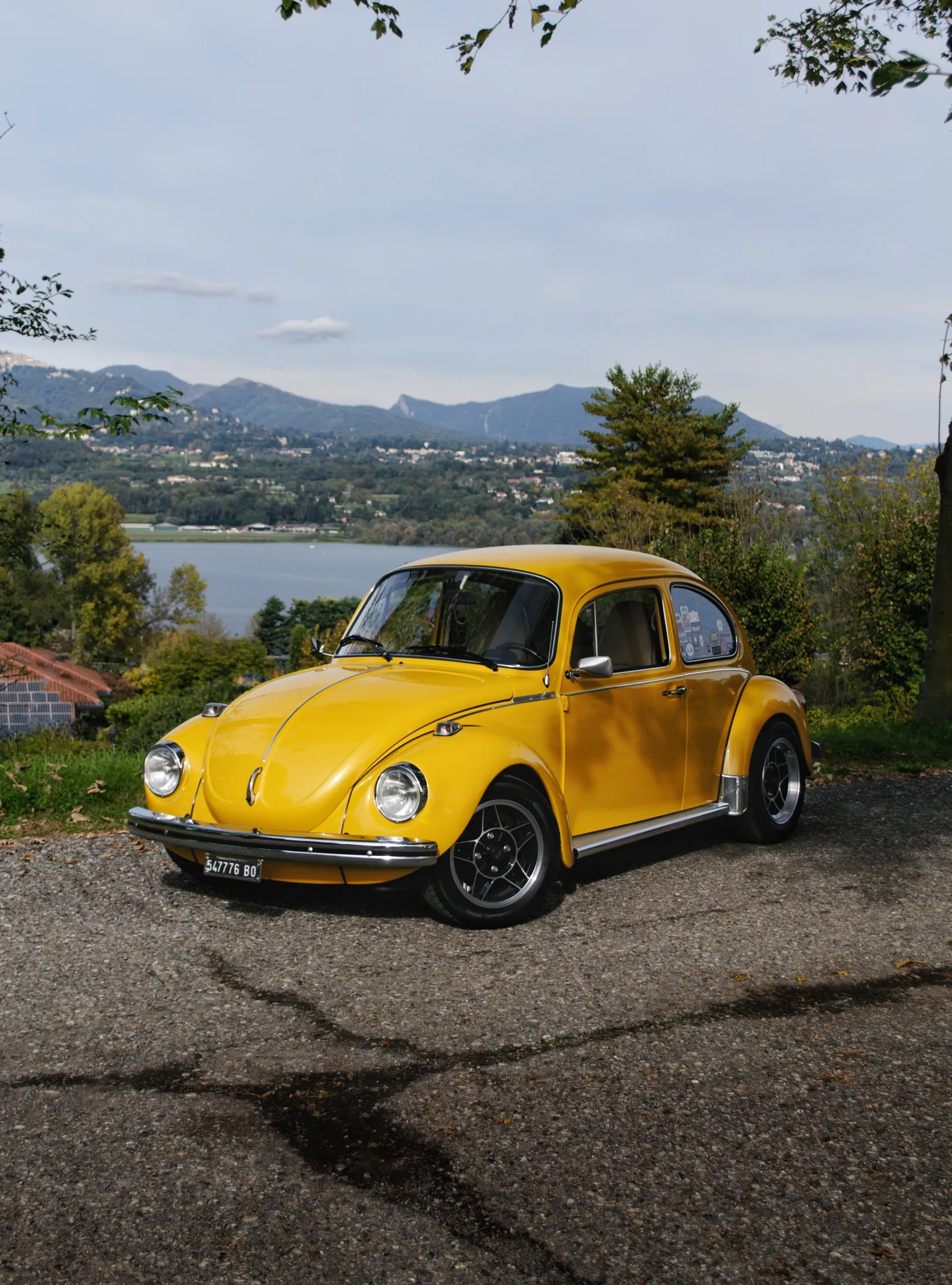 Volkswagen Maggiolino giallo con lago e montagne sullo sfondo